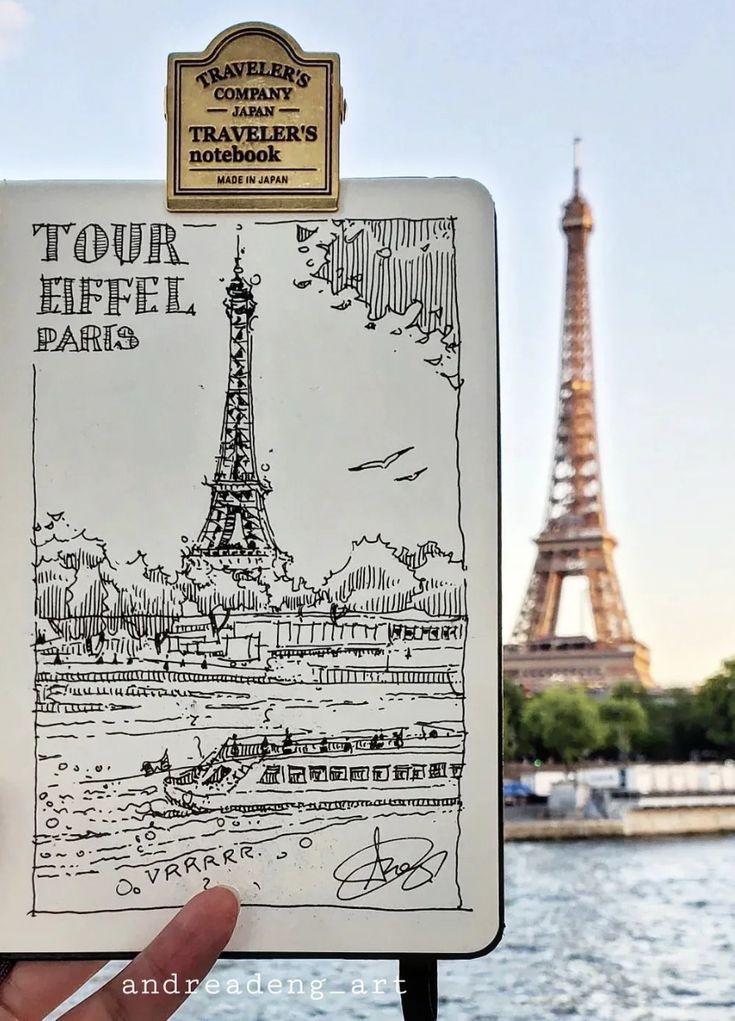 Sketch of Eiffel Tower in a notebook with the real tower in the background. Traveler's notebook by the Seine River.