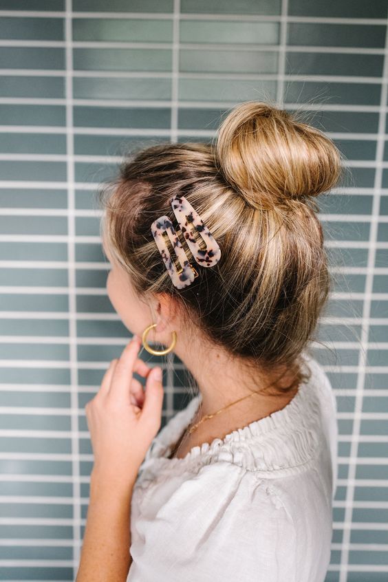 Woman with a bun hairstyle using tortoiseshell hair clips, standing against a blue tiled background.