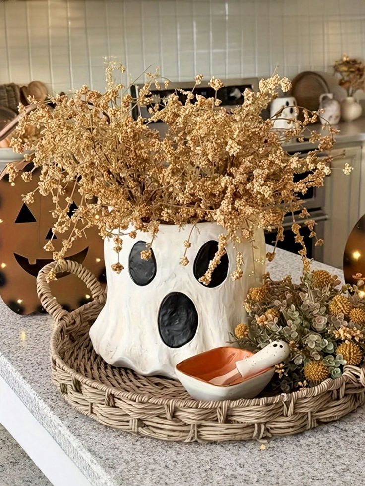 Halloween-themed kitchen decor with ghost-shaped vase, dried flowers, and festive accents on a woven tray.