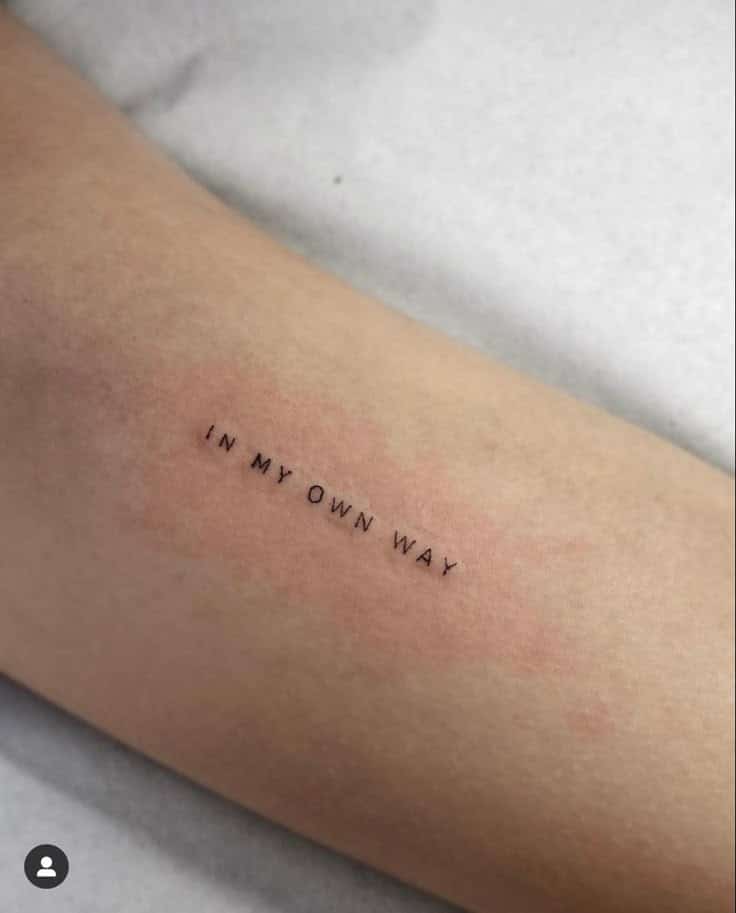 Tattoo on forearm reading IN MY OWN WAY in black ink on light skin. Minimalist text design on arm.