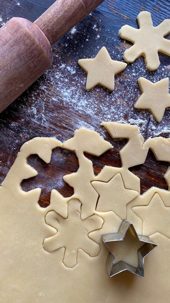 Cookie dough with star and snowflake cutouts, rolling pin and flour on wooden table background. Holiday baking scene.