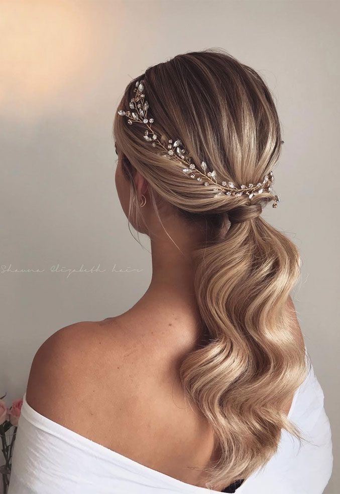 Elegant wavy ponytail hairstyle adorned with a delicate floral hairpiece, perfect for weddings or special occasions.