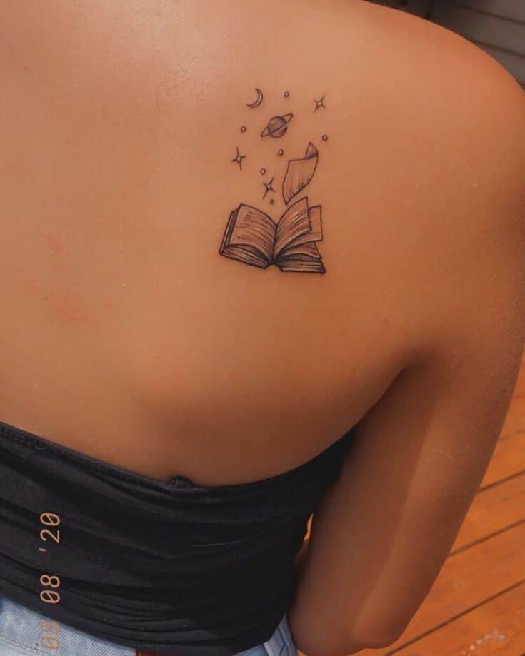 _ 2 Tattoo of open book with floating pages, stars, moon, and planet on a person's shoulder. | Sky Rye Design Tattoo of open book with floating pages, stars, moon, and planet on a person's shoulder.