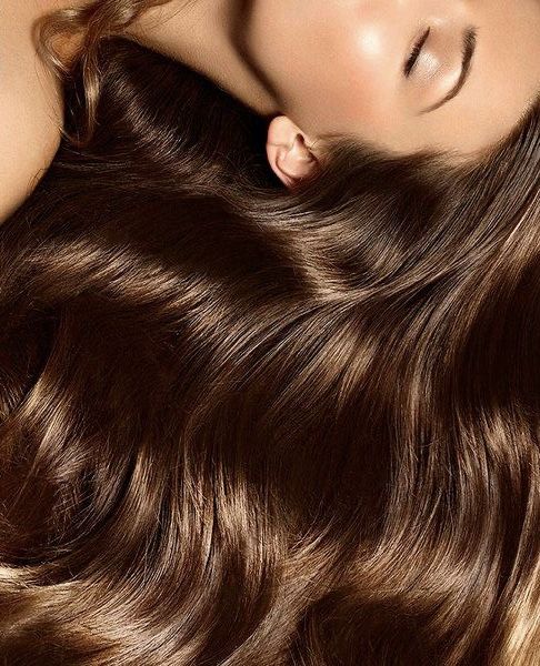 Shiny, healthy brown hair flowing smoothly beneath a serene face with closed eyes, showcasing beauty and hair care.