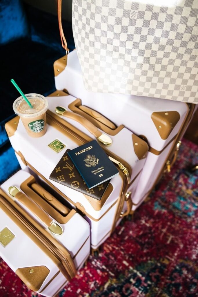 Luxury travel essentials: designer luggage, passport, and iced coffee on a vibrant rug.