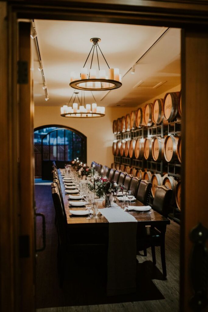 Elegant winery dining room with long table, wine barrels, chandeliers, set for an intimate gathering.