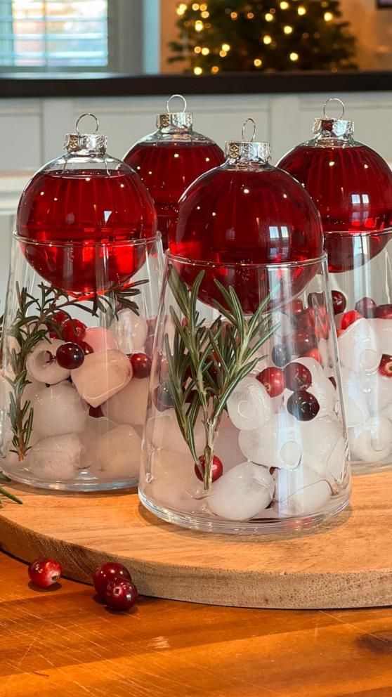 Festive red Christmas ornaments with rosemary and cranberries in glass jars, set on a wooden table.
