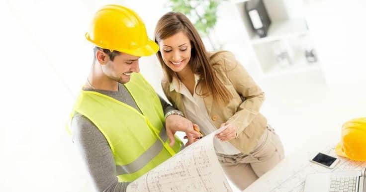 Smiling engineer and architect reviewing blueprints in an office setting.