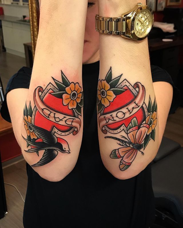 Forearm tattoos with Mom and Dad banners, flowers, a swallow, and a butterfly in a traditional style.
