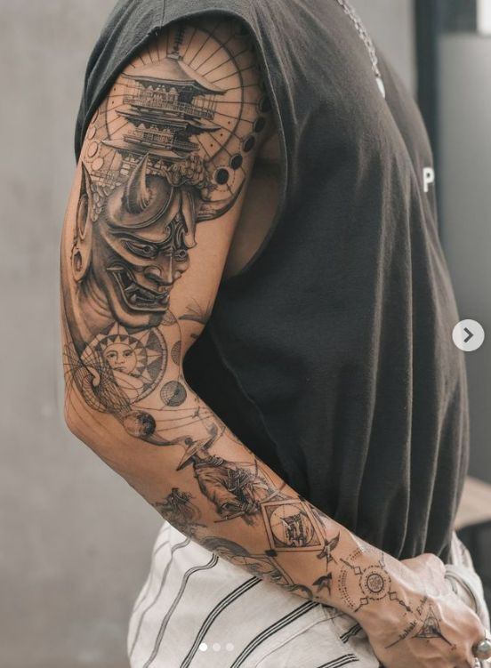 Arm tattoo featuring intricate Japanese demon mask design with celestial and geometric elements, black ink.