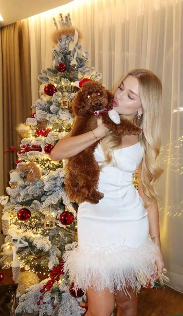 Woman in white dress with brown dog in front of a decorated Christmas tree.
