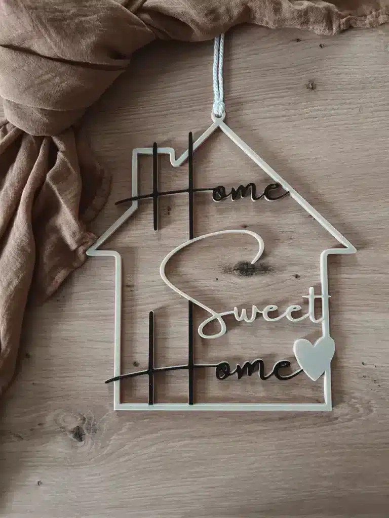 Hanging decoration reads Home Sweet Home on a wooden background, styled in a house shape with a heart accent.