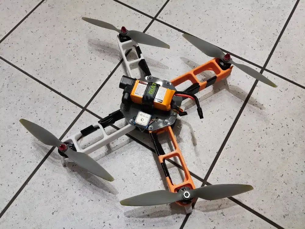 DIY quadcopter drone on tiled floor, featuring orange and white frame and four propellers.