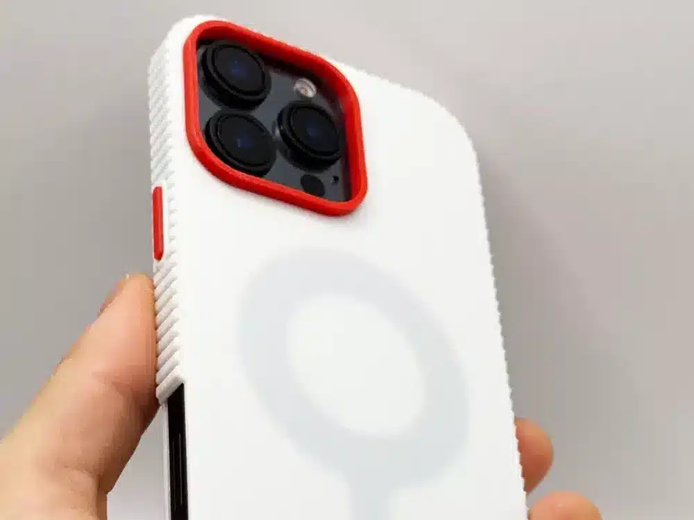 White smartphone with red-accented case, featuring a circular design, held in a hand against a neutral background.