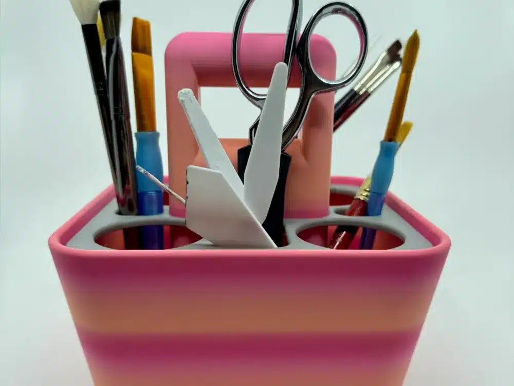 Artistic tools in a pink holder including brushes, scissors, and a crafting knife, organized for creative projects.