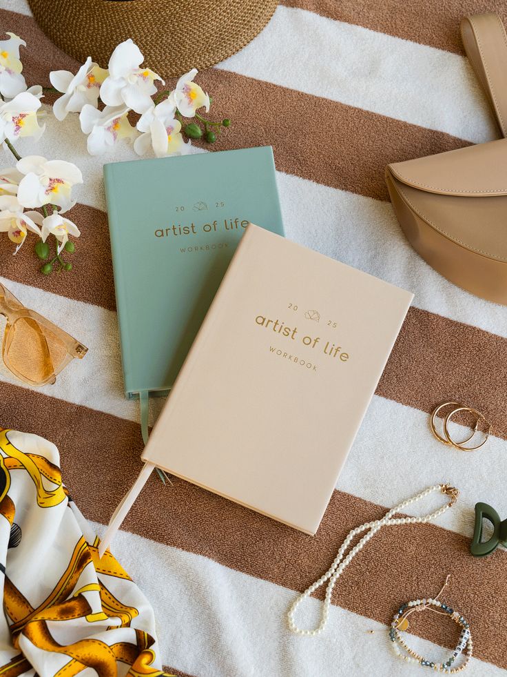 Artist of Life workbooks on a striped blanket with orchids, sunglasses, and accessories.
