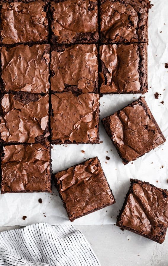 Fudgy brownies with crackly tops arranged on parchment paper, perfect dessert treats.