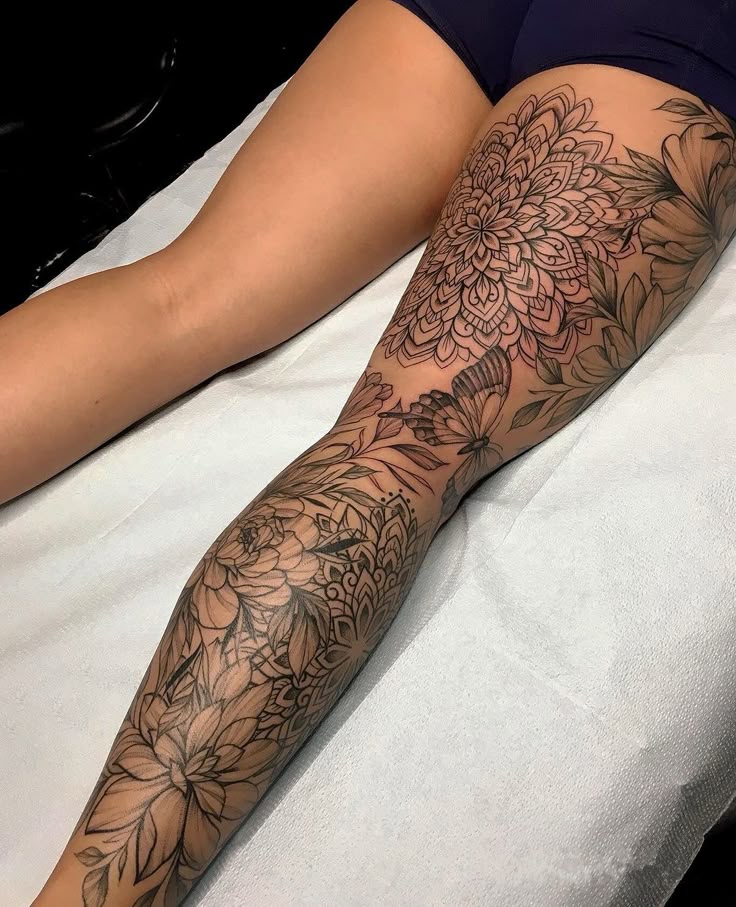 _ 21 Person with an intricate floral and butterfly tattoo sleeve on their leg, showcasing detailed black and grey designs. | Sky Rye Design Person with an intricate floral and butterfly tattoo sleeve on their leg, showcasing detailed black and grey designs.
