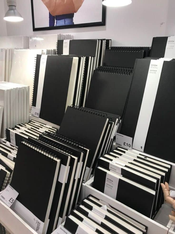 Display of black sketchbooks and notebooks in various sizes, neatly organized on shelves under bright lighting in a store.