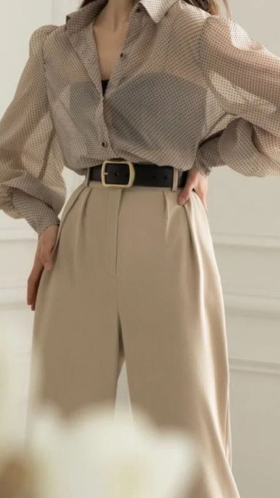 Woman in sheer polka-dot blouse and beige pants with black belt, stylish modern fashion.