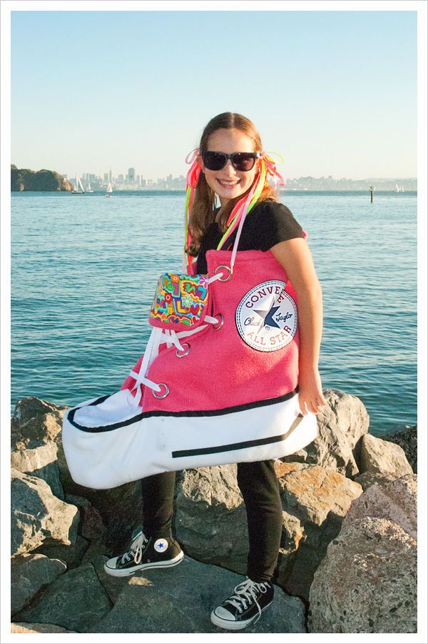 Person in a giant pink sneaker costume by the sea, wearing sunglasses and smiling.
