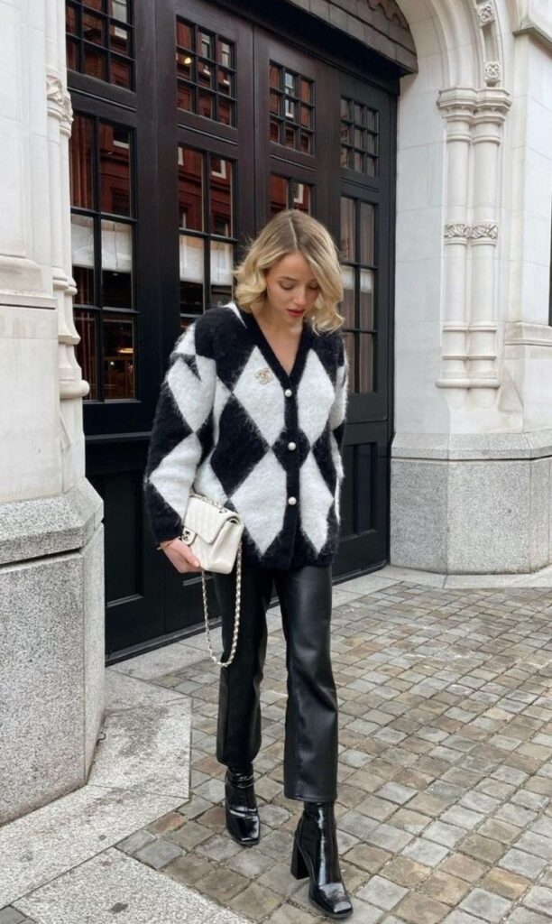 _ 22 Fashionable woman in black and white diamond sweater, leather pants, and boots by an elegant building. | Sky Rye Design Fashionable woman in black and white diamond sweater, leather pants, and boots by an elegant building.