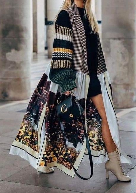 Fashionable woman in a colorful patchwork coat and boots, holding a chic black handbag.