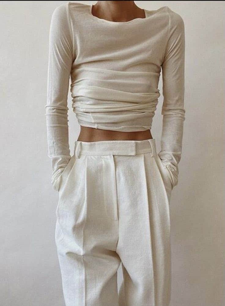 Fashionable woman in cream top and wide-leg trousers, hands in pockets, showcasing minimalist style.