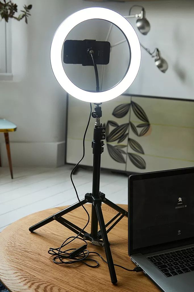Ring light on tripod with smartphone and laptop, ideal for vlogging or video calls in a home setup.
