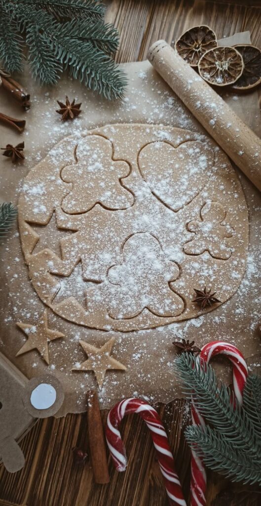 _ 24 Baking Christmas cookies with shapes on dough, surrounded by rolling pin, cinnamon, candy canes, and pine branches. | Sky Rye Design Baking Christmas cookies with shapes on dough, surrounded by rolling pin, cinnamon, candy canes, and pine branches.