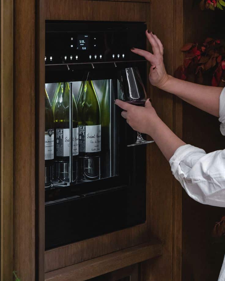 24_ Built-In Wine Dispenser Person using a wine dispenser to pour a glass of white wine from a wooden cabinet. | Sky Rye Design Person using a wine dispenser to pour a glass of white wine from a wooden cabinet.