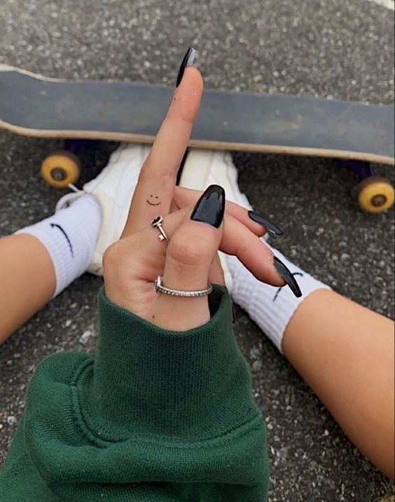 24b823bce463251ba8c6a5a8ebcdbfc6 Person sitting with skateboard, wearing black nails, green hoodie, and smiley face hand tattoo, displaying rings. | Sky Rye Design Person sitting with skateboard, wearing black nails, green hoodie, and smiley face hand tattoo, displaying rings.
