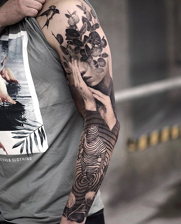 Arm tattoo featuring abstract face, nature elements, and bird, on person wearing a graphic shirt.