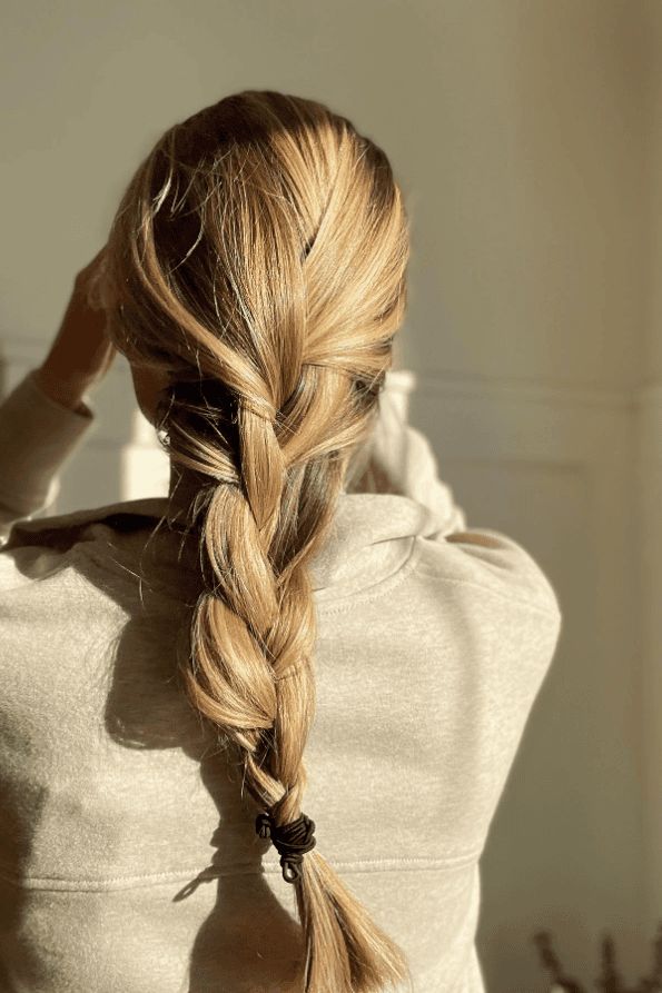 Blonde woman with braided hair in the sun, wearing a beige sweater, facing away.