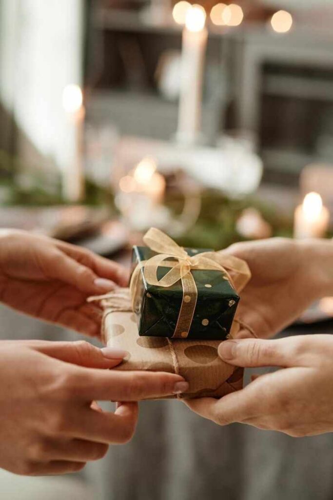 Hands exchanging beautifully wrapped gifts at a festive candlelit gathering, emphasizing holiday joy and warmth.
