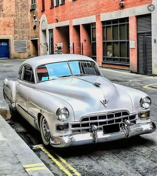 Classic silver car parked in an urban alley, showcasing vintage design and chrome details.