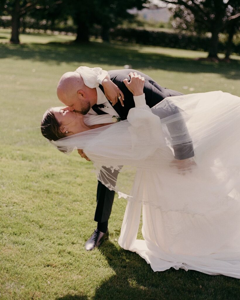 Bride and groom kissing in a romantic garden setting on their wedding day.