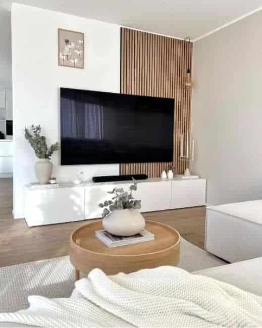 Modern living room with large TV, white cabinet, wooden accents, and decor on a coffee table. Cozy, minimalist design.