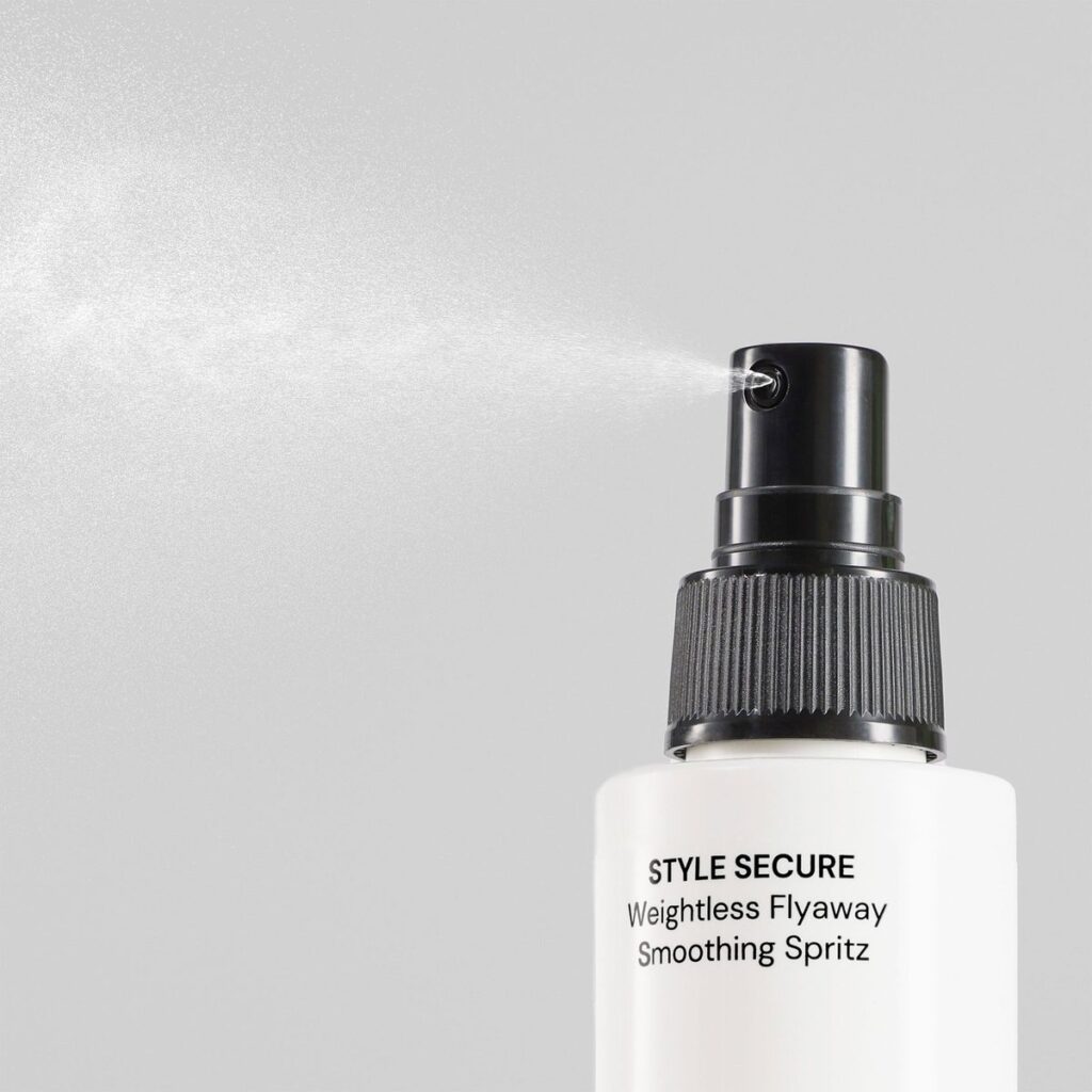 Hair spray bottle releasing mist. Text reads STYLE SECURE Weightless Flyaway Smoothing Spritz. Gray background.
