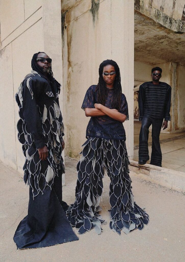 Group wearing avant-garde fashion with layered designs in a rustic setting.