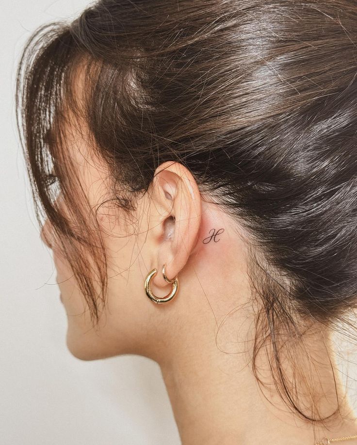 2812e469860f951ca7d6e9e0fe627c49 Side profile showing small ear tattoo of letter behind ear, with gold hoop earrings. | Sky Rye Design Side profile showing small ear tattoo of letter behind ear, with gold hoop earrings.