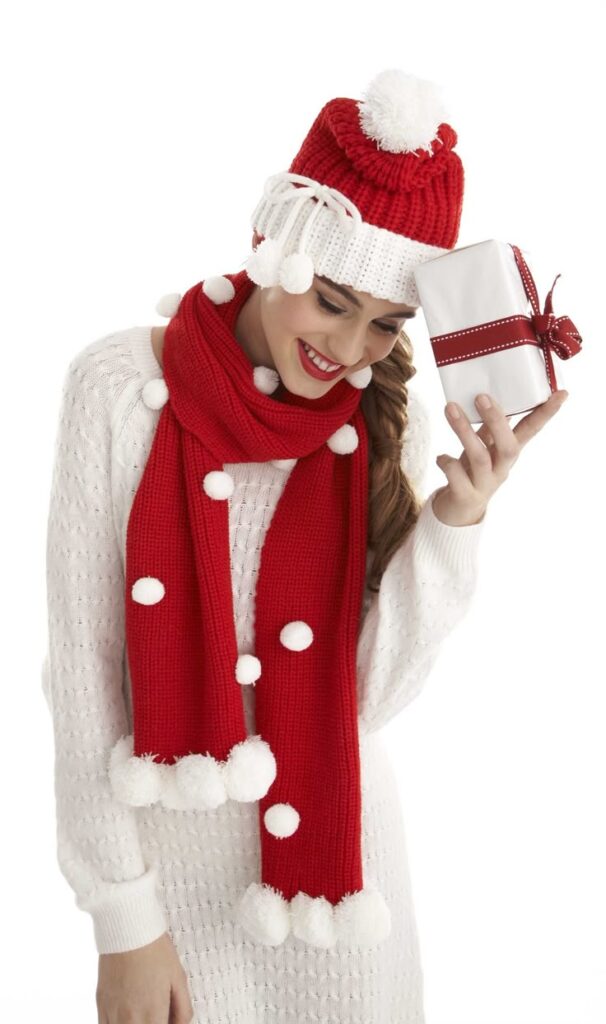 Woman in festive red and white winter outfit holding a wrapped gift with ribbon, smiling. Cozy holiday fashion.