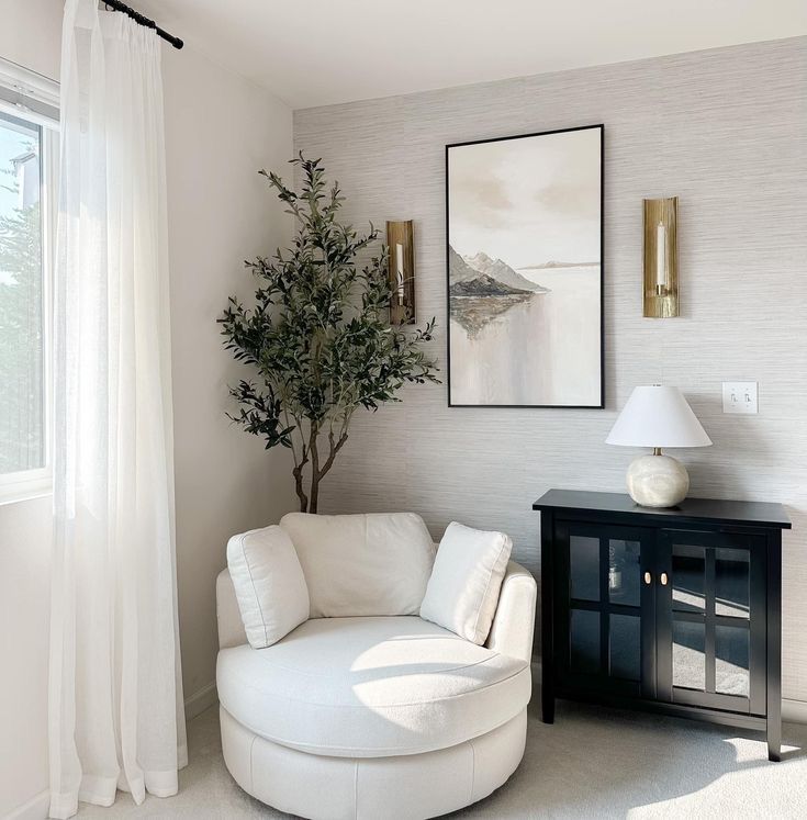 Cozy reading nook with white round chair, leafy plant, art, and cabinet in a bright, minimalist room.