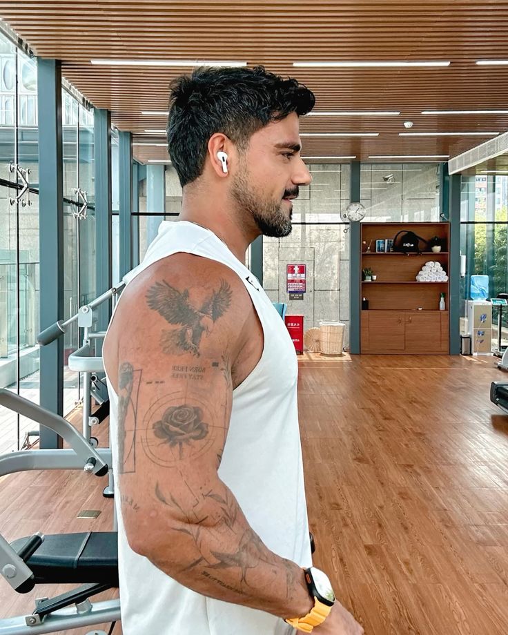 2c5c7064e280941449e0f446f8fdcca6 Man with tattoos wearing earbuds at the gym, in a bright, modern workout space. | Sky Rye Design Man with tattoos wearing earbuds at the gym, in a bright, modern workout space.