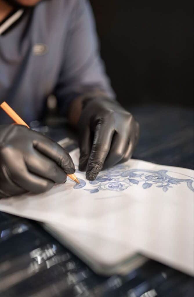 Tattoo artist wearing gloves sketching detailed flower design on paper.