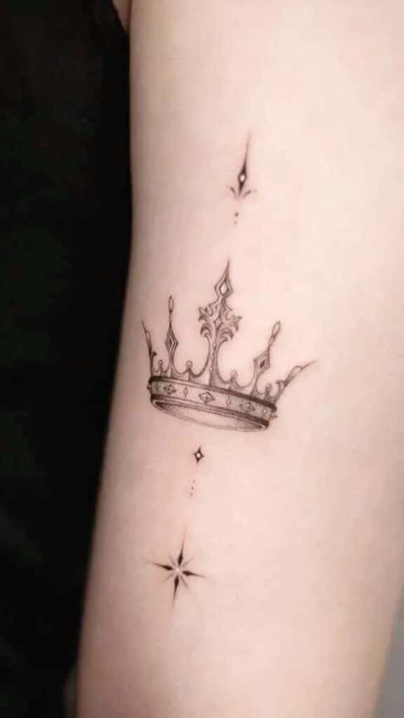 _ 3 Elegant crown tattoo with sparkling stars on forearm, showcasing intricate and minimalist design. | Sky Rye Design Elegant crown tattoo with sparkling stars on forearm, showcasing intricate and minimalist design.