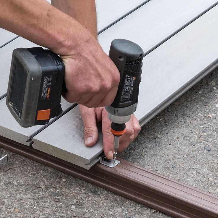 _ 3 Person using a drill to fasten composite decking boards securely onto a metal frame outdoors. | Sky Rye Design Person using a drill to fasten composite decking boards securely onto a metal frame outdoors.