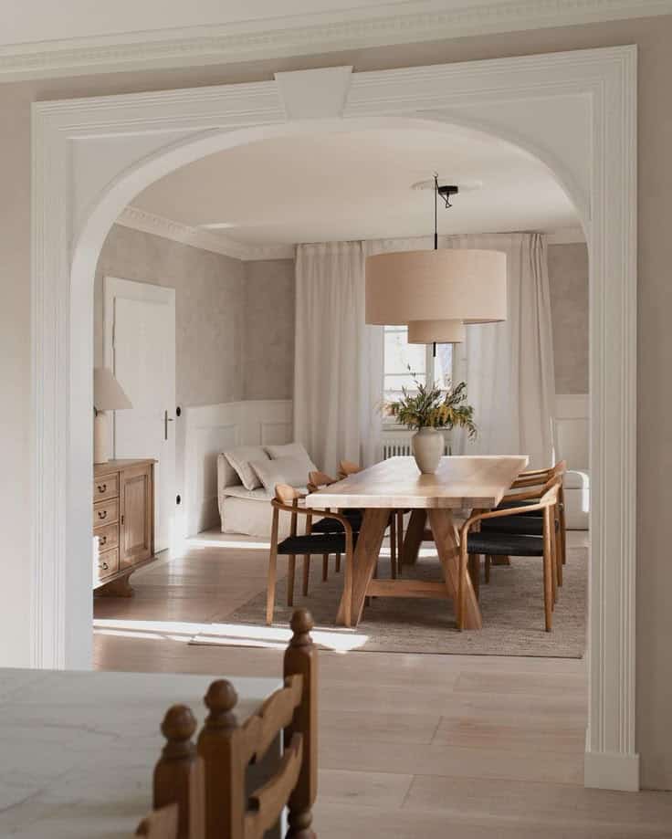 Cozy dining room with wooden table, chairs, elegant archway, and neutral decor, creating a warm, inviting atmosphere.