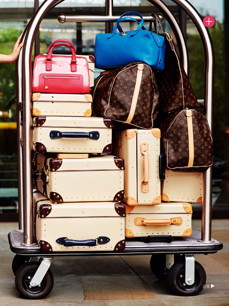 Luxury luggage and handbags stacked on hotel cart, featuring designer brand and vibrant colors.