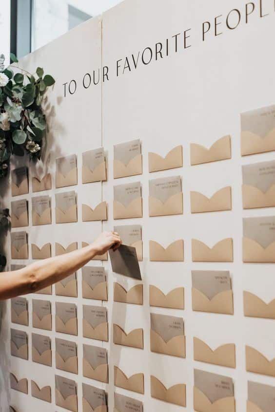 Wedding seating chart display with envelopes labeled 'To Our Favorite People,' hand reaching for a card.